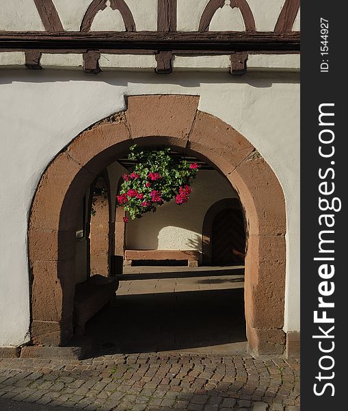 The outside of a town hall in a southern German town is made of a half-timbered structure and an old arch with a pot-flower hanging in its middle. The outside of a town hall in a southern German town is made of a half-timbered structure and an old arch with a pot-flower hanging in its middle.