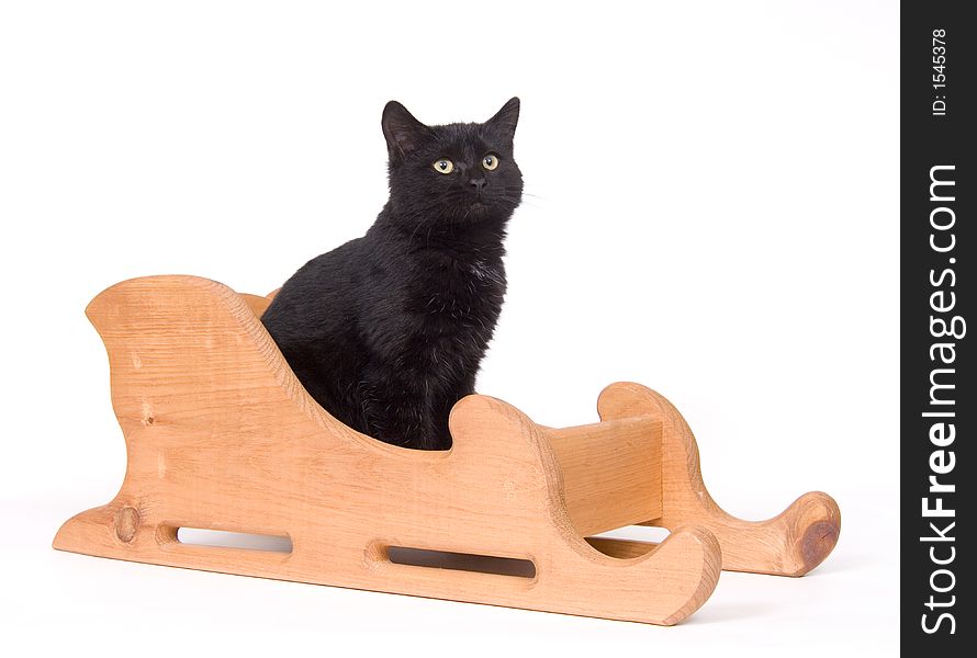 A black cat sits in a wooden sled on a white background. A black cat sits in a wooden sled on a white background