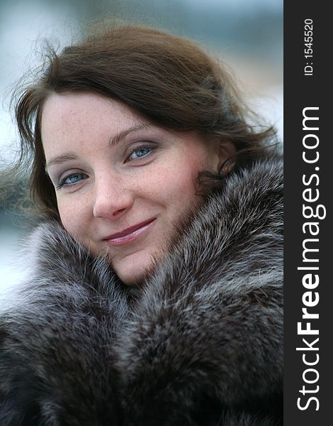 Portrait of a smiling beautiful girl in a fur coat from a raccoon on the nature