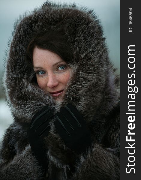 Portrait of a smiling beautiful girl in a fur coat from a raccoon on the nature