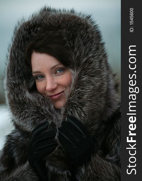 Portrait of a smiling beautiful girl in a fur coat from a raccoon on the nature