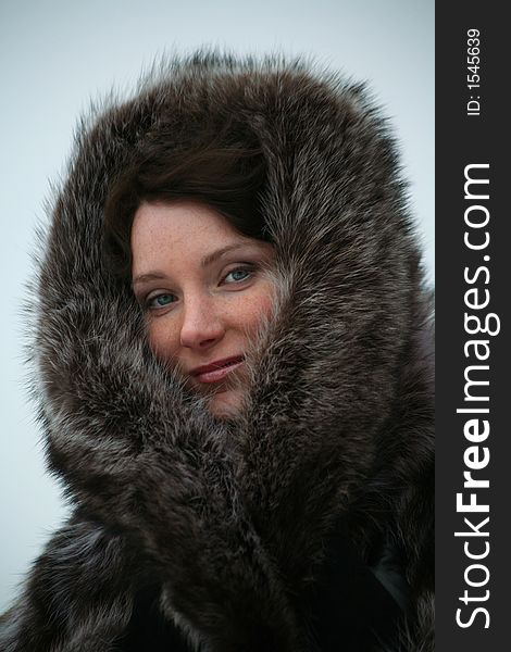 Portrait of a smiling beautiful girl in a fur coat from a raccoon on the nature