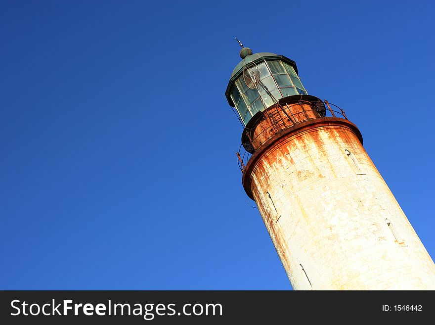 Old rusted lighthouse in front a clear blue sky.