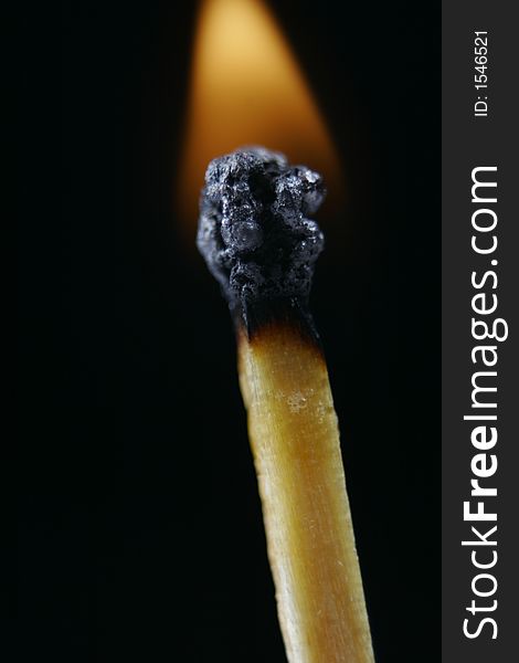Match head on fire against black background with norrow focus on match head