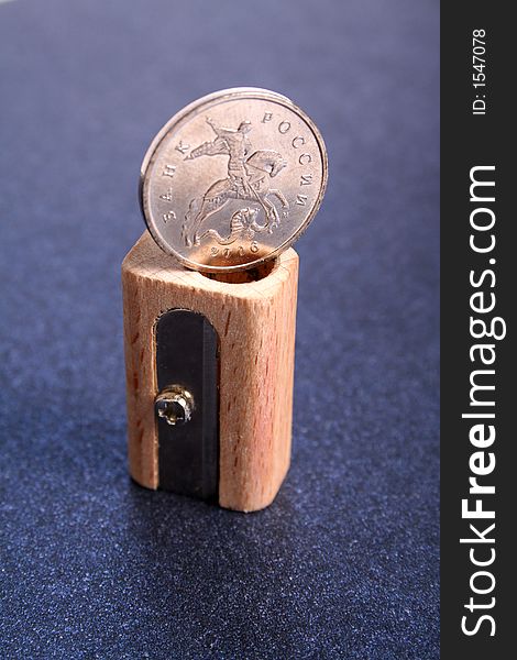 The Russian coin on a sharpener for pencils made of wood on a color paper