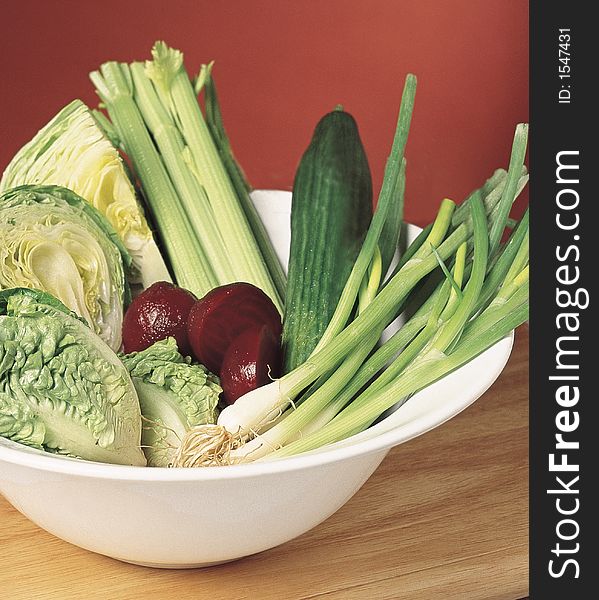 A salad bowl containing spring onions, cucumber, beetroot, celery and lettuce