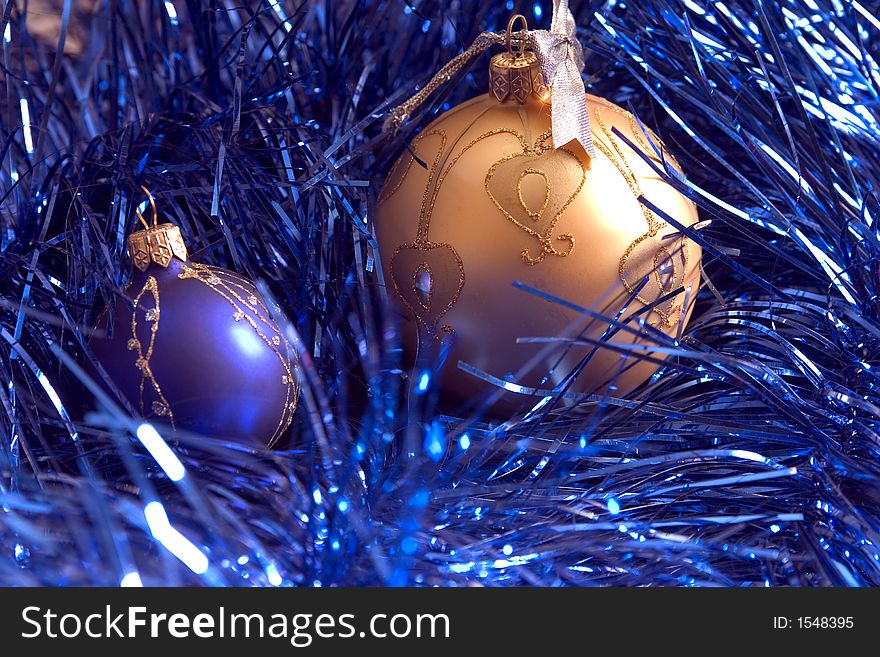 A yellow and blue fir-tree balls lies on blue new-year tinsel on a white background