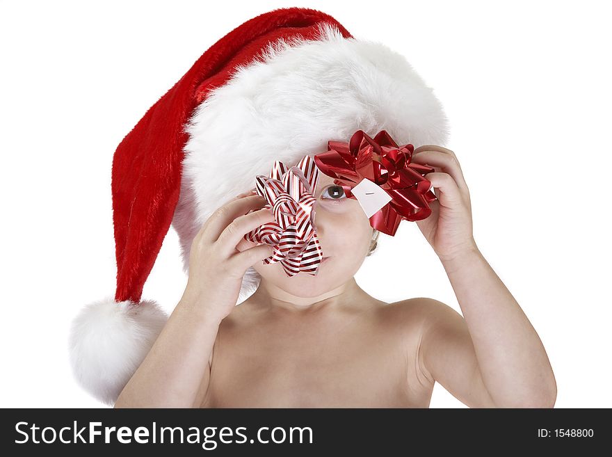 A young child wearing a santa hat and holding a red christmas bow and a red & white christmas bow. Looking at the camera though the bows, the white sticker underneath is visible. Isolated white background. A young child wearing a santa hat and holding a red christmas bow and a red & white christmas bow. Looking at the camera though the bows, the white sticker underneath is visible. Isolated white background