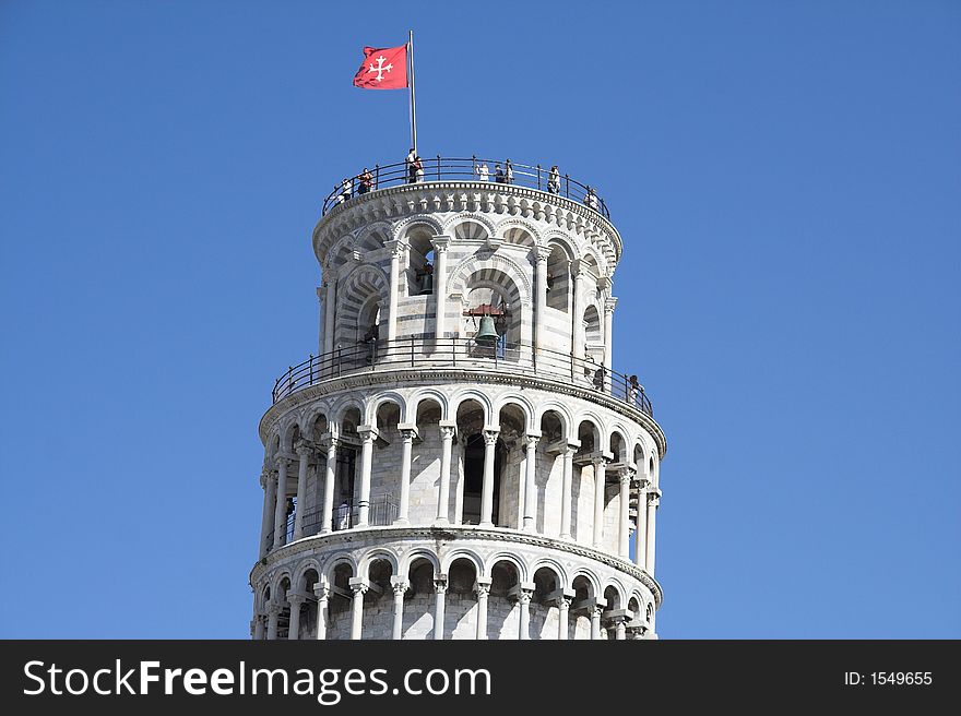 The top of tower of pisa with flag and tourists