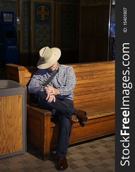 Senior man sitting on a wooden bench in the sun light at a train station waiting for his train. Senior man sitting on a wooden bench in the sun light at a train station waiting for his train