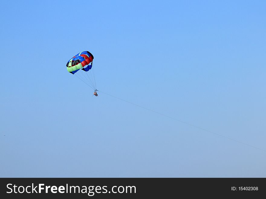 Parasailing over open water with blue sky background and buildings on shoreline in the distance.