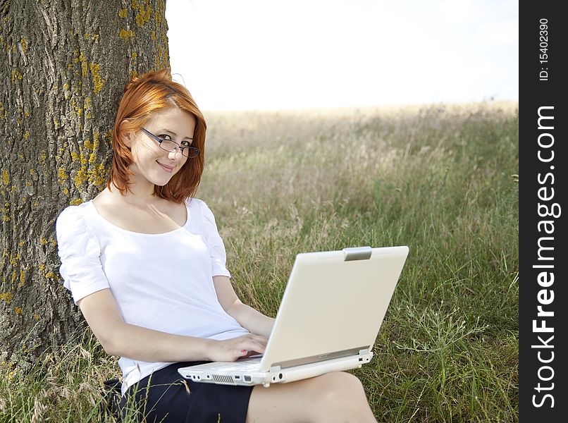 Young Businesswomen in white with glasses and laptop sitting near tree.