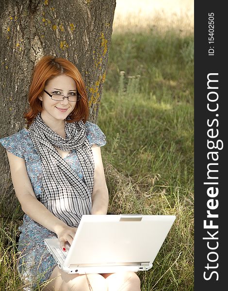 Young smiling fashion girl in glasses and notebook sitting near tree. Young smiling fashion girl in glasses and notebook sitting near tree.