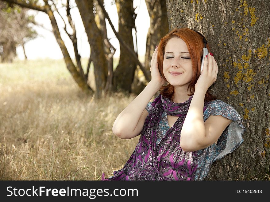 Young smiling girl with headphones near tree. Outdoor photo.