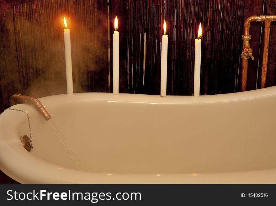 Water pouring into vintage bath from bronze tap with four candles preparing for romantic bath. Water pouring into vintage bath from bronze tap with four candles preparing for romantic bath