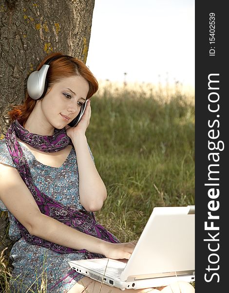 Young smiling fashion girl with notebook and headphones sitting near tree. Young smiling fashion girl with notebook and headphones sitting near tree.