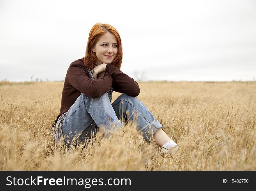 Beautiful red-haired girl at yellow autumn grass. Outdoor photo.