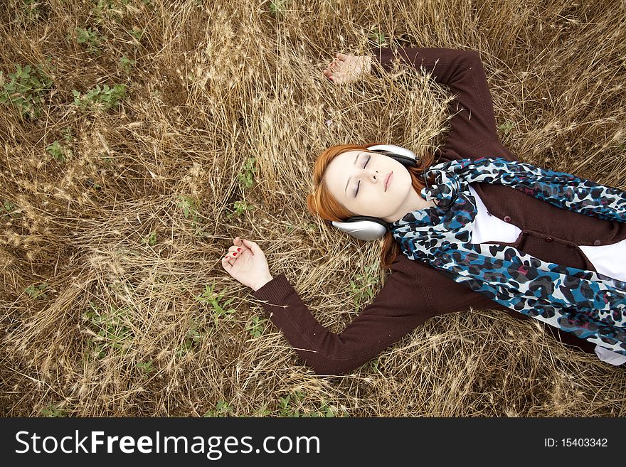 Young girl with headphones lying at field.