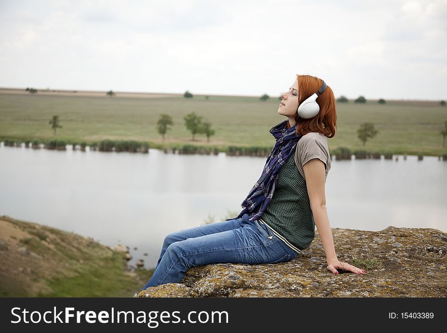 Young fashion girl with headphones at rock near lake. Young fashion girl with headphones at rock near lake.