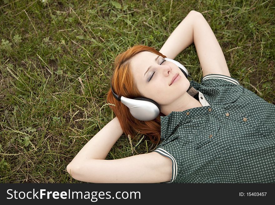 Young fashion girl with headphones lying at green grass.