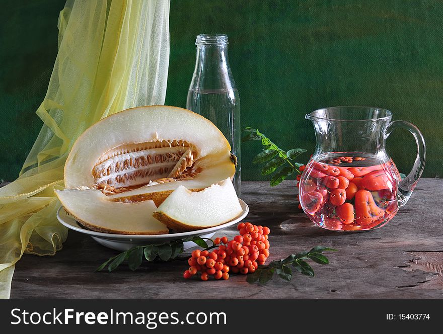 on an old table in a dish melon, alongside wild ash, glass jug and fabric. on an old table in a dish melon, alongside wild ash, glass jug and fabric