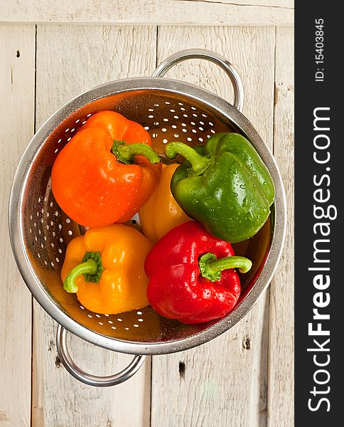 Five bell peppers in a colander on a wooden background