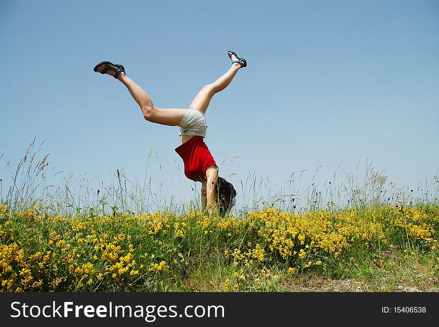 Young woman doing a cartwheel in a meadow with yellow flowers