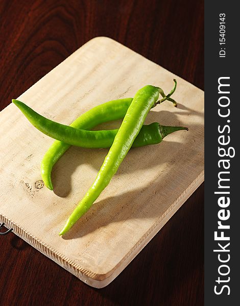 Dramatic lighting of three green chilis on wooden chopping board