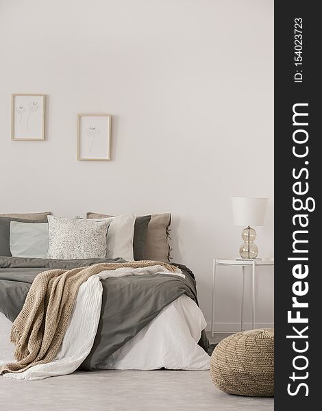 Stylish white lamp on simple nightstand table next to warm bed with cozy grey bedding