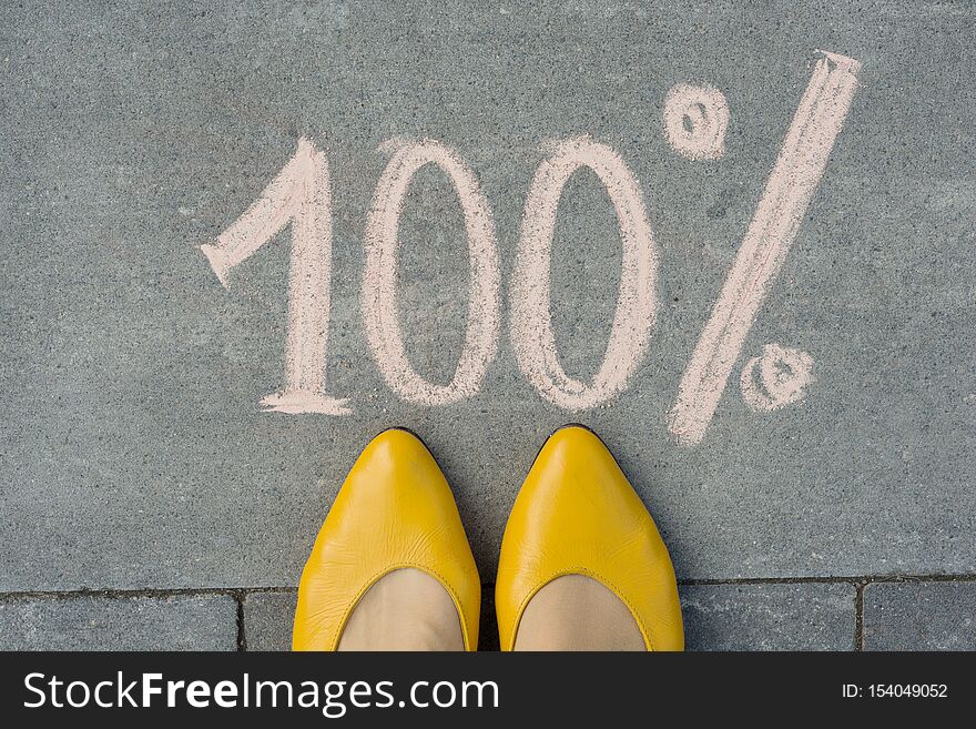 Female feet with text 100 percent written on grey sidewalk