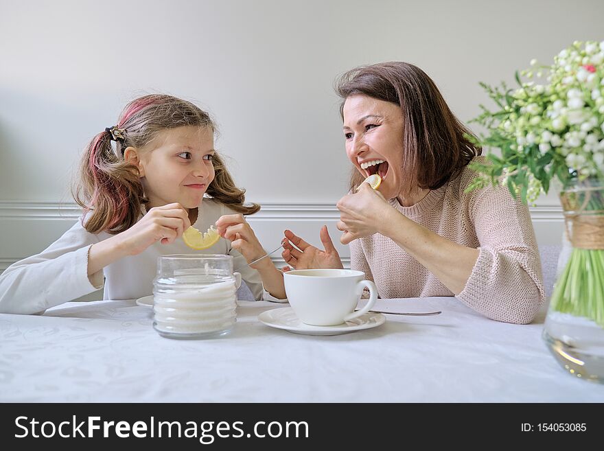 Laughing mother and daughter drinking from cups and eating lemon