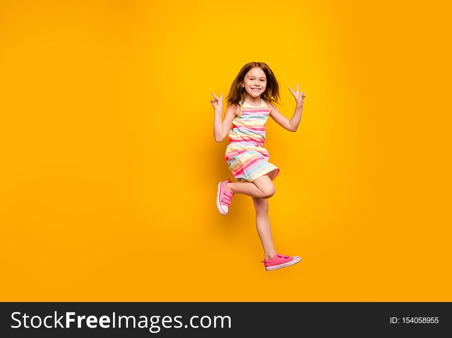 Full size photo of cheerful kid, jumping making v-signs isolated over yellow background