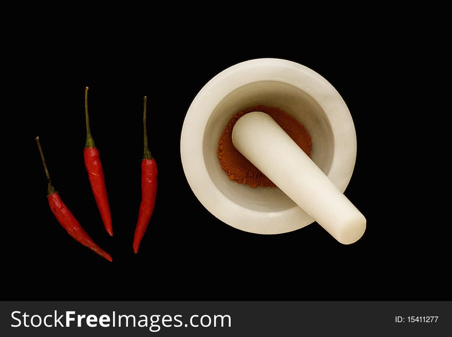 3 chillis and some chilli powder in a mortar and pestle on a black background. 3 chillis and some chilli powder in a mortar and pestle on a black background