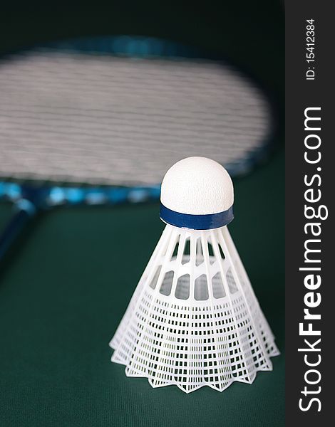 A white synthetic shuttlecock and a blue badminton racquet on a green background. A white synthetic shuttlecock and a blue badminton racquet on a green background.