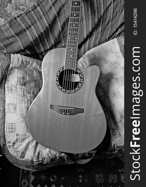An acoustic guitar in black and white against a background of cushions and fabric. An acoustic guitar in black and white against a background of cushions and fabric