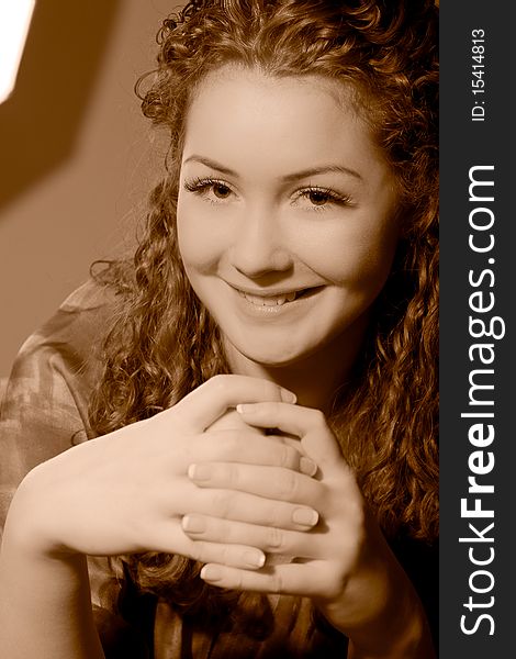 Young pretty smiling caucasian girl with natural beautiful curly hair sitting in front of wall and laughing made in sepia tonality. Young pretty smiling caucasian girl with natural beautiful curly hair sitting in front of wall and laughing made in sepia tonality