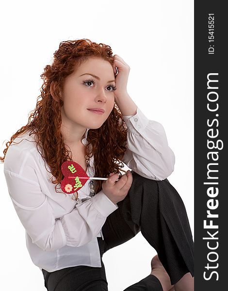 Caucasian pretty red haired girl with colorful bon-bon sitting with smiling facial expression and dreaming isolated on white background. Caucasian pretty red haired girl with colorful bon-bon sitting with smiling facial expression and dreaming isolated on white background
