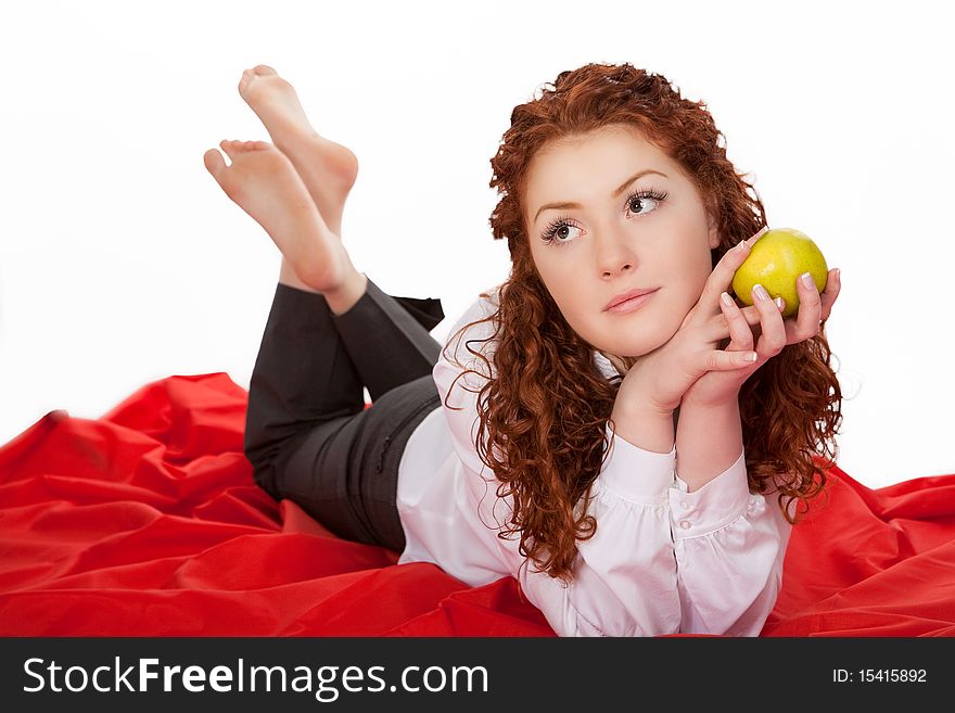 Relaxing cute caucasian red haired girl with green apple having calm time lying on floor upon a red carpet isolated on white background. Relaxing cute caucasian red haired girl with green apple having calm time lying on floor upon a red carpet isolated on white background