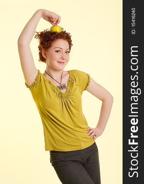 Happy and good looking young caucasian girl with red hair having fun time with apple holding it on top of the head standing isolated. Happy and good looking young caucasian girl with red hair having fun time with apple holding it on top of the head standing isolated
