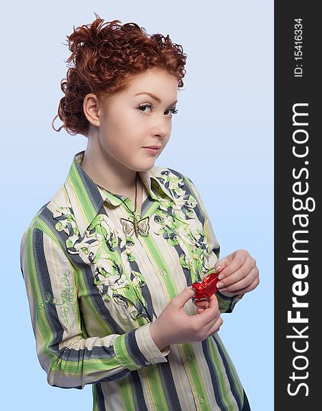 Calm and beautiful young red haired girl with curly natural hair unwraping chokolate candy bar standing with curious facial expression and isolated over light blue background. Calm and beautiful young red haired girl with curly natural hair unwraping chokolate candy bar standing with curious facial expression and isolated over light blue background