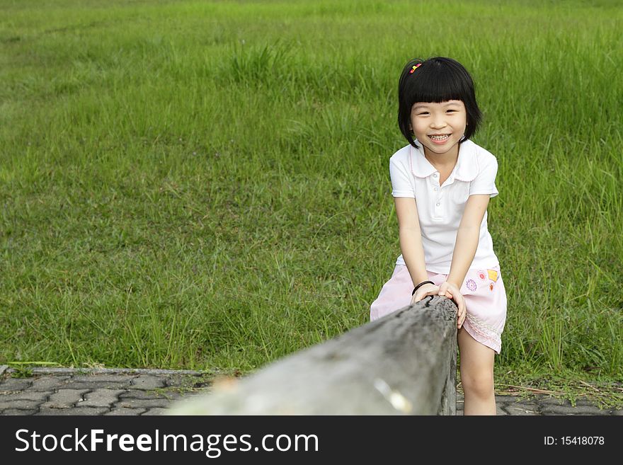 An Asian girl sitting on a wooden beam at a park