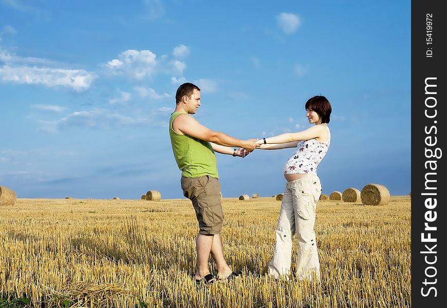 Young couple is staying in the meadow and hold on their hands. Woman is pregnant. Young couple is staying in the meadow and hold on their hands. Woman is pregnant.