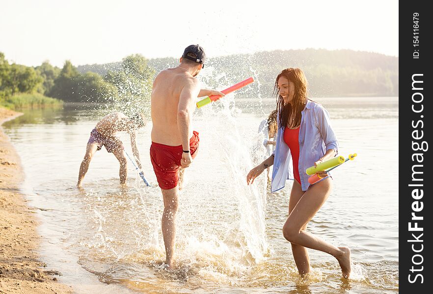 Happy people with water guns have fun on the beach