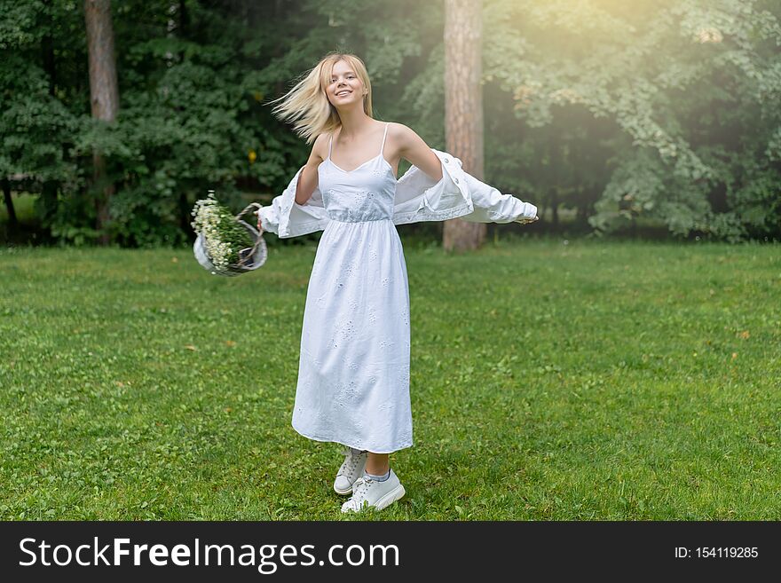 Beautiful Young Woman Outdoors holding basket with daisies. Enjoy Nature. Healthy Smiling Girl in Green Grass. Copyspace