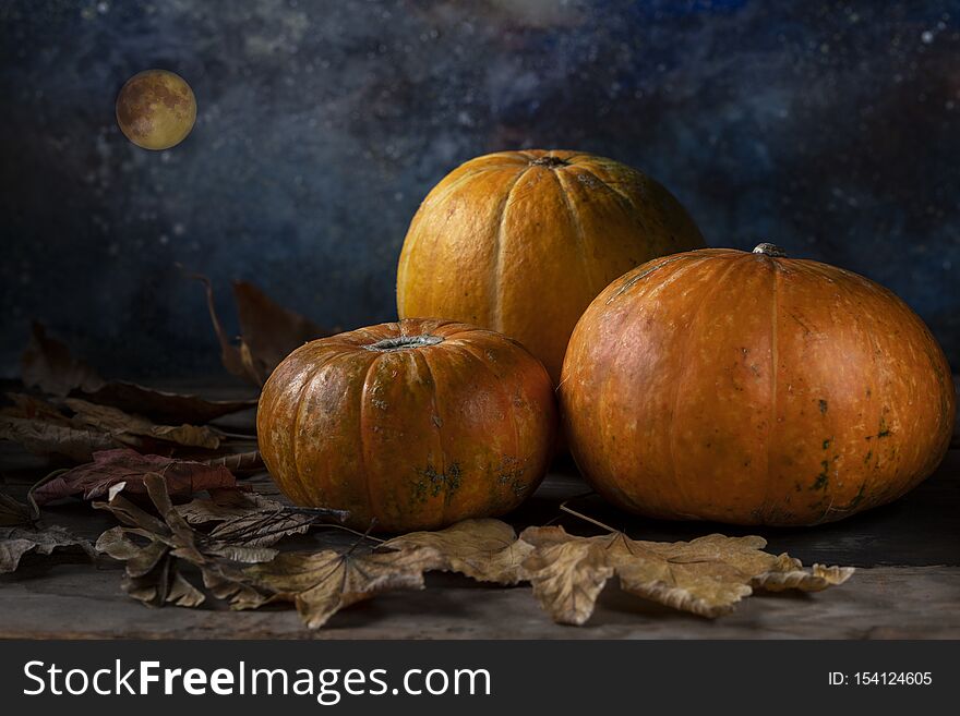 A group of three pumpkins and fallen dry leaves