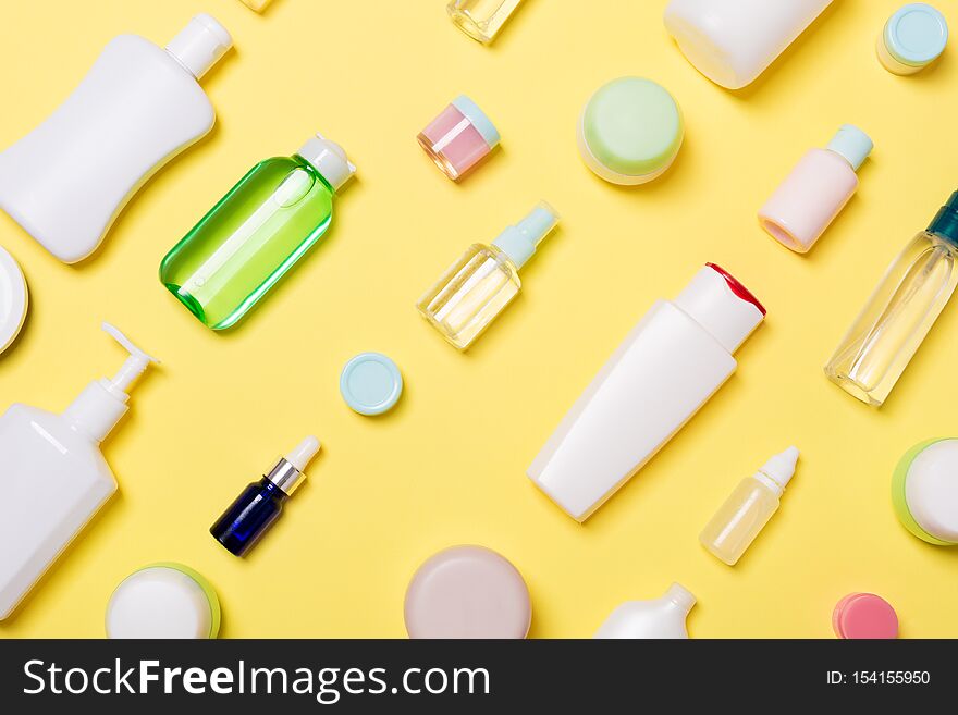 Top view of different cosmetic bottles and container for cosmetics on yellow background. Flat lay composition with copy space