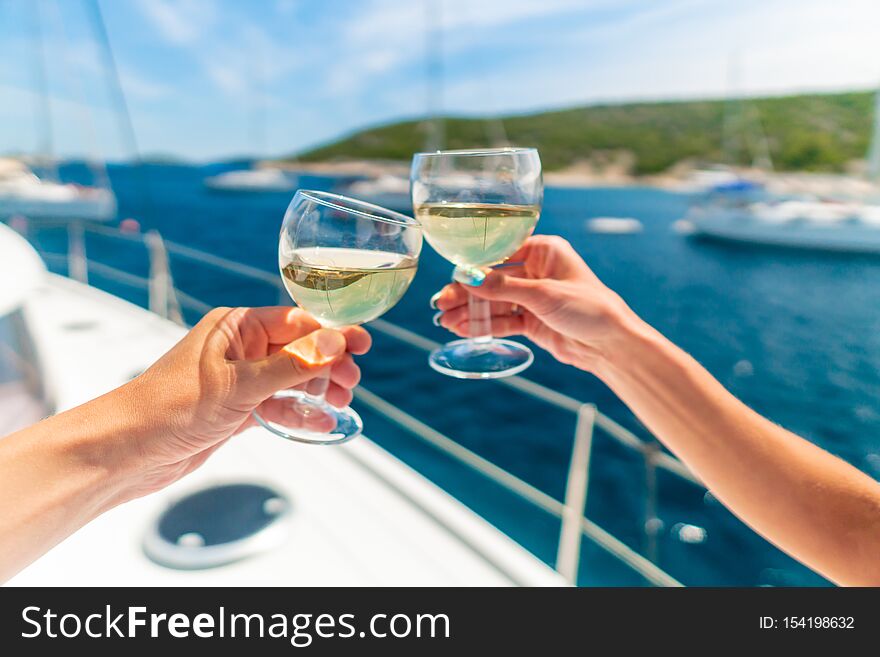 Couple holding two glasses of white wine over ocean background with yacht on background - shallow depth of field