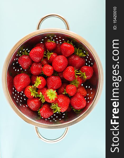 Ripe strawberries in a colander with a blue background