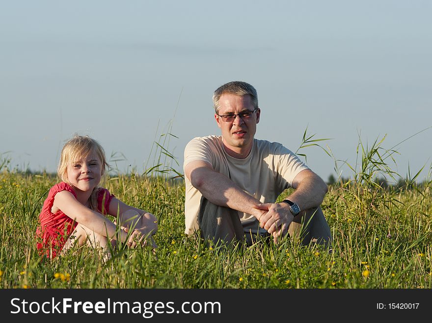 Father With Daughter Sit On Meadow