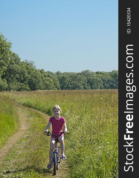 Little girl on bicycle on meadow in summer